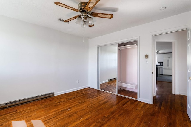 unfurnished bedroom featuring a closet, wood finished floors, built in fridge, and baseboard heating