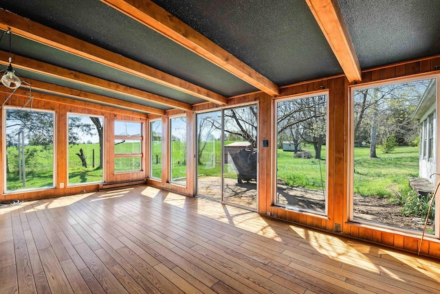unfurnished sunroom featuring wooden walls, a wooden deck, beamed ceiling, and wood finished floors