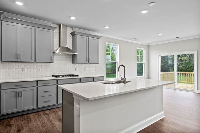 kitchen with ornamental molding, gray cabinets, stainless steel gas stovetop, wall chimney exhaust hood, and a sink