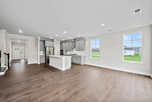 kitchen featuring visible vents, gray cabinetry, wall chimney range hood, open floor plan, and stainless steel fridge