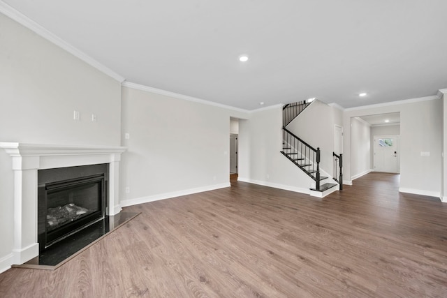 unfurnished living room with a glass covered fireplace, wood finished floors, crown molding, baseboards, and stairs