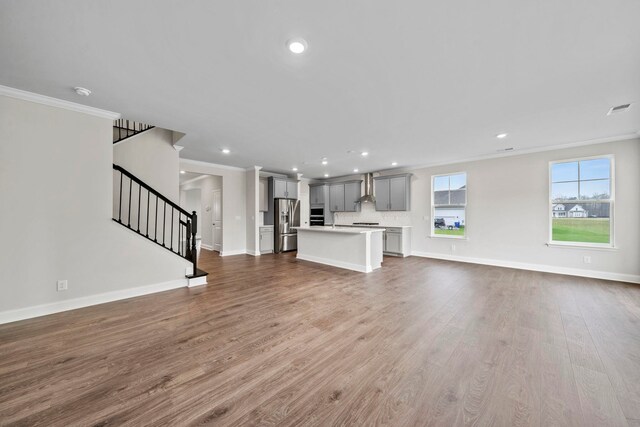 unfurnished living room with stairs, crown molding, wood finished floors, and baseboards