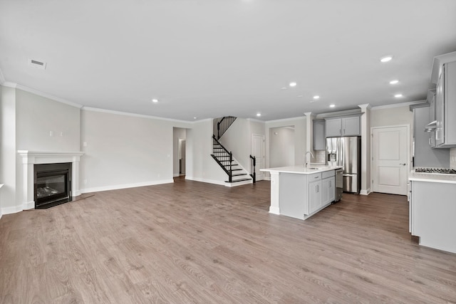 unfurnished living room with a glass covered fireplace, recessed lighting, light wood finished floors, baseboards, and stairs