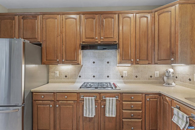 kitchen featuring backsplash, brown cabinets, appliances with stainless steel finishes, and exhaust hood