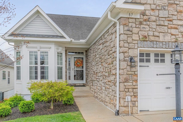 doorway to property featuring an attached garage, roof with shingles, and stone siding