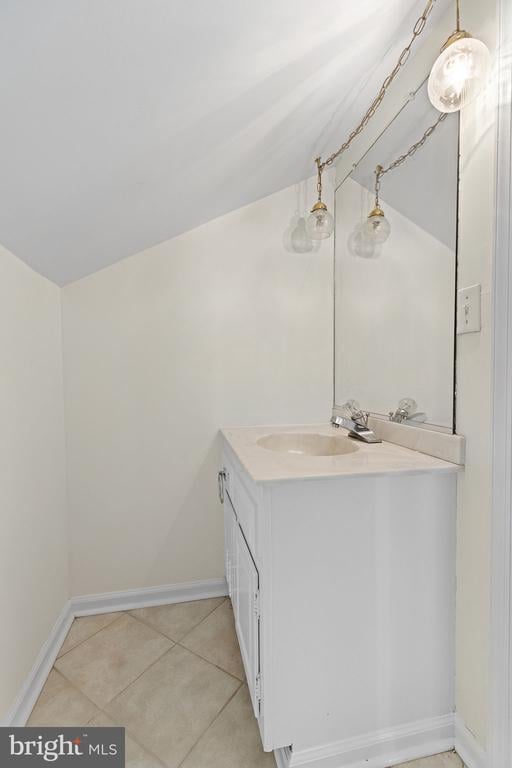 bathroom with tile patterned flooring, baseboards, vanity, and lofted ceiling