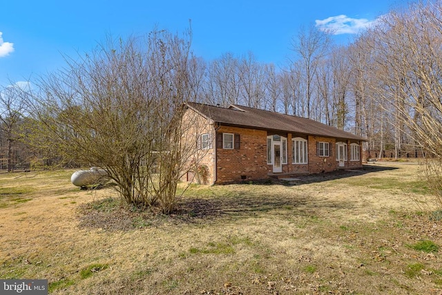 view of side of property with crawl space, a yard, brick siding, and roof with shingles