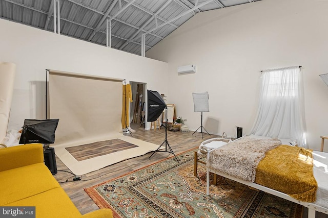 bedroom featuring a wall unit AC, wood finished floors, and high vaulted ceiling