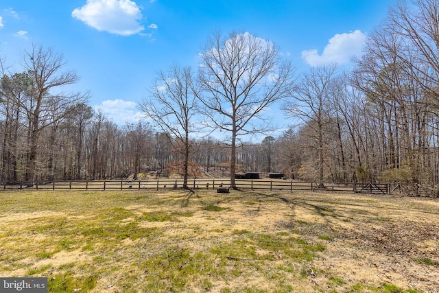 view of yard with a rural view, a wooded view, and fence