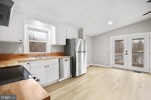 kitchen featuring stainless steel appliances, a sink, white cabinetry, light wood-style floors, and vaulted ceiling