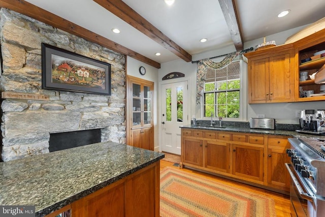 kitchen with high end range, sink, a stone fireplace, and dark stone counters