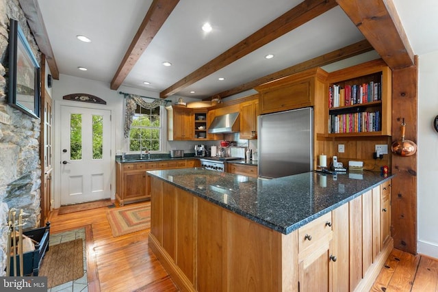 kitchen with range, dark stone countertops, built in refrigerator, light hardwood / wood-style floors, and wall chimney exhaust hood