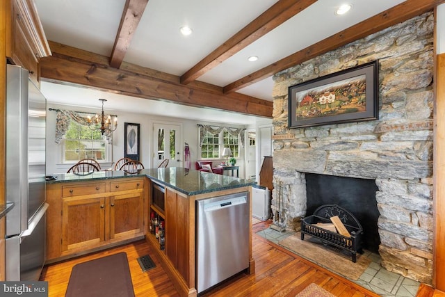 kitchen featuring appliances with stainless steel finishes, dark stone countertops, hardwood / wood-style floors, decorative light fixtures, and kitchen peninsula