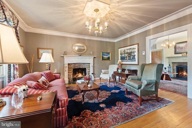 living room featuring wood-type flooring, crown molding, a notable chandelier, and a fireplace