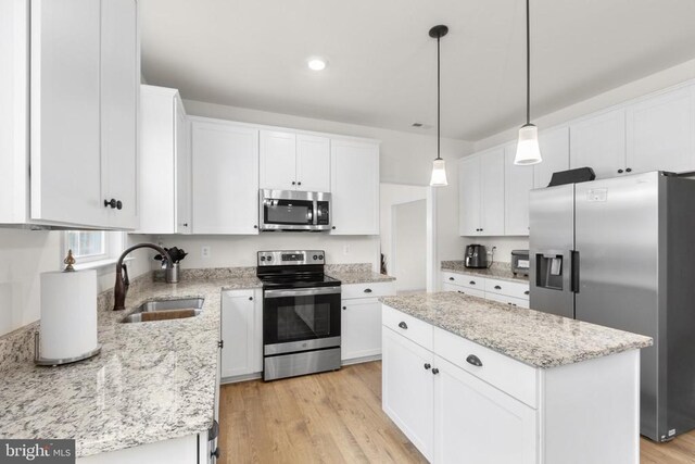 kitchen with light wood-style flooring, appliances with stainless steel finishes, white cabinetry, a sink, and a center island