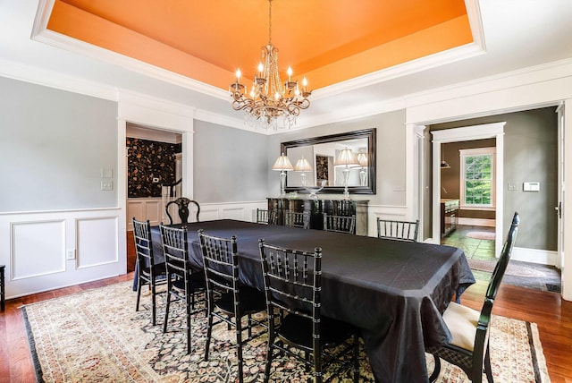 dining area with crown molding, wood-type flooring, a raised ceiling, and a notable chandelier