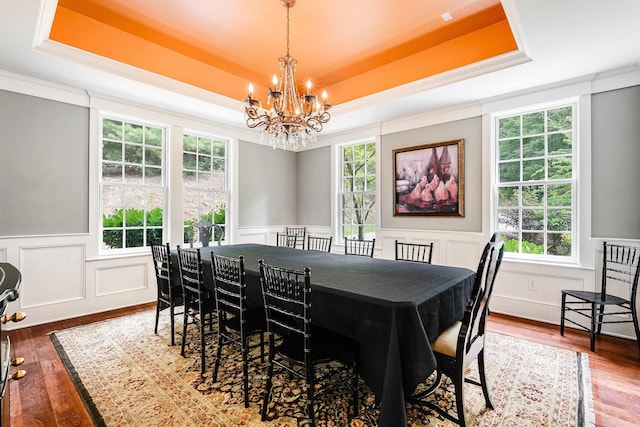 dining space with a raised ceiling, crown molding, hardwood / wood-style floors, and a notable chandelier