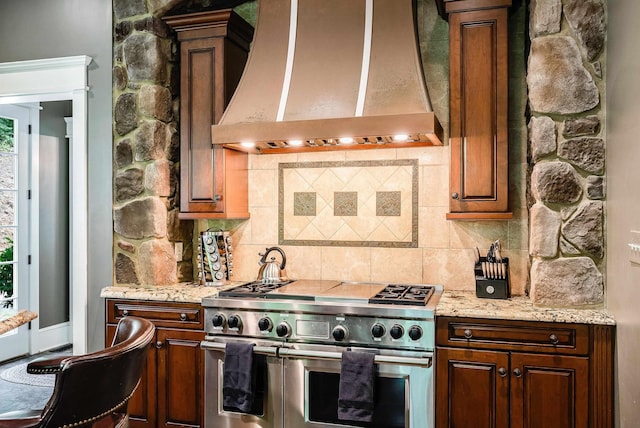 kitchen featuring premium range hood, tasteful backsplash, light stone counters, and range with two ovens