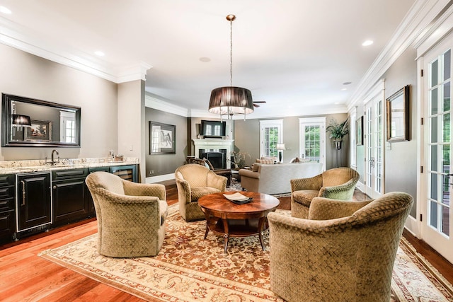 living room featuring wet bar, ornamental molding, light hardwood / wood-style floors, and french doors