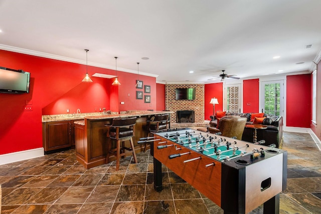 rec room featuring ornamental molding, indoor bar, ceiling fan, and a brick fireplace