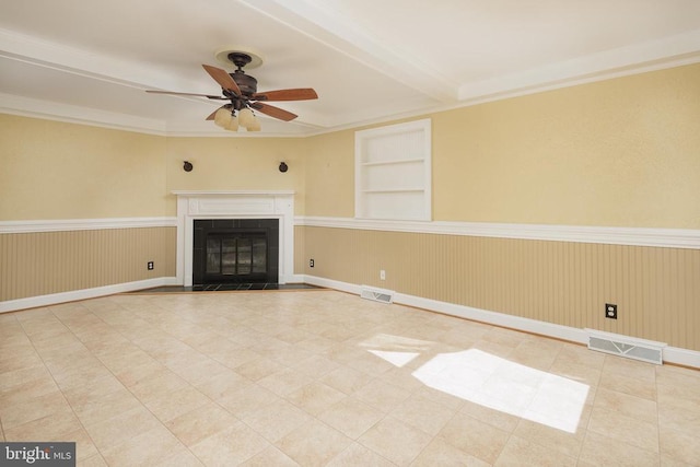 unfurnished living room featuring a tile fireplace, ornamental molding, ceiling fan, beam ceiling, and built in shelves