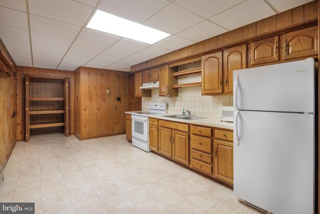 kitchen with white appliances, wooden walls, a paneled ceiling, and sink