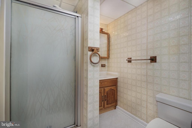 bathroom featuring a shower with door, tile walls, vanity, tile patterned floors, and toilet