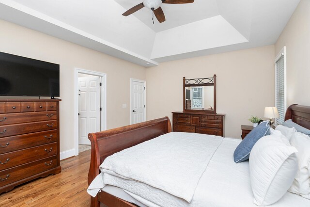 bedroom with ceiling fan, a raised ceiling, and light wood-type flooring