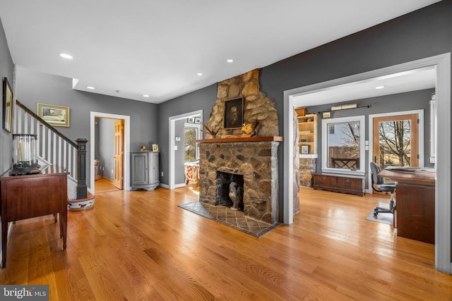 living area featuring recessed lighting, a stone fireplace, wood finished floors, baseboards, and stairs