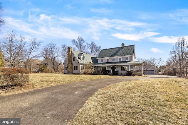 view of front of property featuring driveway, a chimney, metal roof, a porch, and a front yard