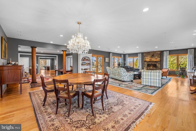 dining space featuring light wood finished floors, a fireplace, recessed lighting, and ornate columns