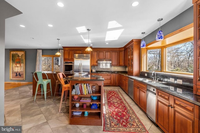 kitchen with under cabinet range hood, stainless steel appliances, a sink, open shelves, and a center island with sink