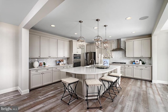 kitchen with appliances with stainless steel finishes, a breakfast bar, wood finished floors, light countertops, and wall chimney range hood