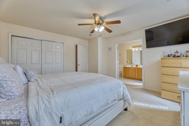 bedroom with ensuite bathroom, light carpet, a ceiling fan, baseboards, and a closet