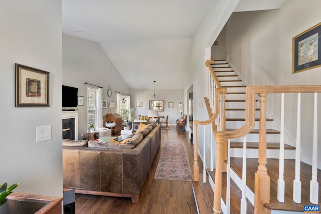 living area with dark wood finished floors, a glass covered fireplace, high vaulted ceiling, and stairs