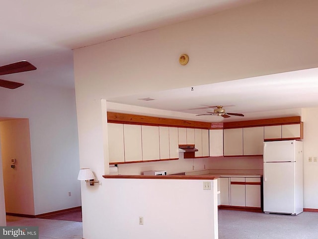 kitchen with a ceiling fan, under cabinet range hood, freestanding refrigerator, a peninsula, and baseboards