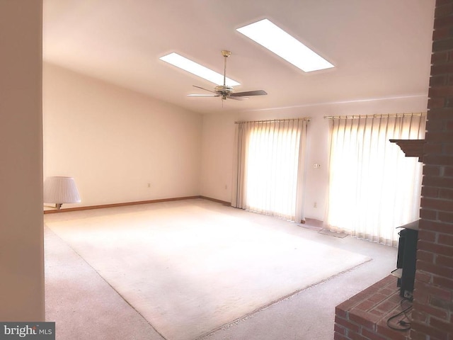 unfurnished living room featuring vaulted ceiling with skylight, carpet, a wood stove, and ceiling fan