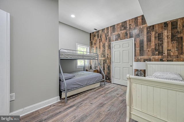 bedroom featuring wooden walls, recessed lighting, wood finished floors, and baseboards