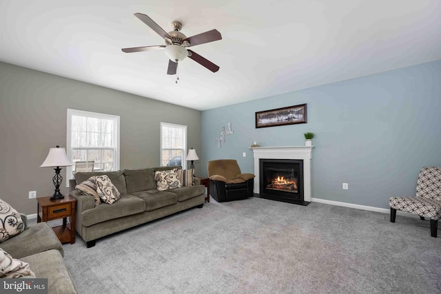 living area featuring a fireplace with flush hearth, baseboards, ceiling fan, and light colored carpet