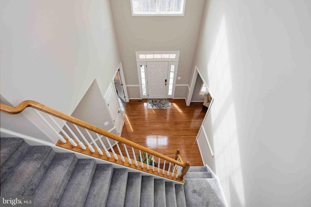 stairs with baseboards, a high ceiling, wood finished floors, and a healthy amount of sunlight