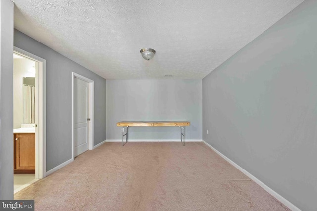 spare room with baseboards, a textured ceiling, and light colored carpet