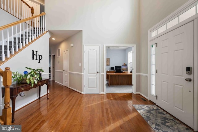 foyer entrance featuring stairway, baseboards, light wood-style flooring, and a towering ceiling