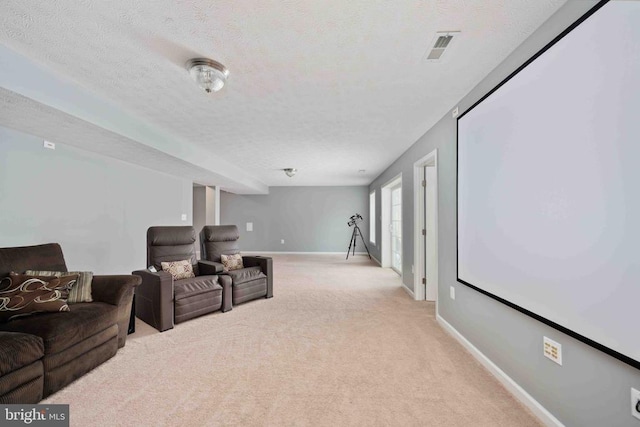 cinema room featuring visible vents, light colored carpet, a textured ceiling, and baseboards