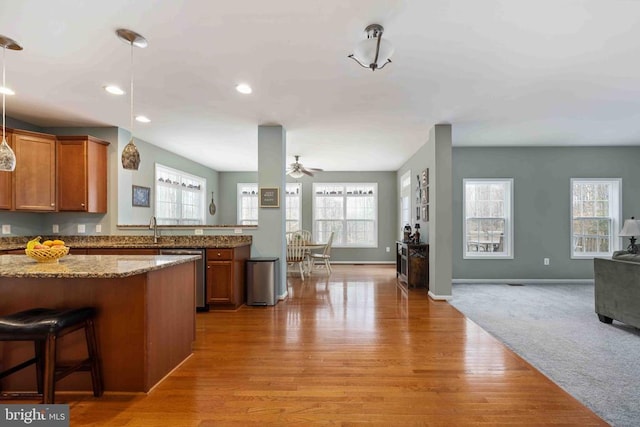 kitchen with light stone counters, open floor plan, hanging light fixtures, stainless steel dishwasher, and brown cabinetry