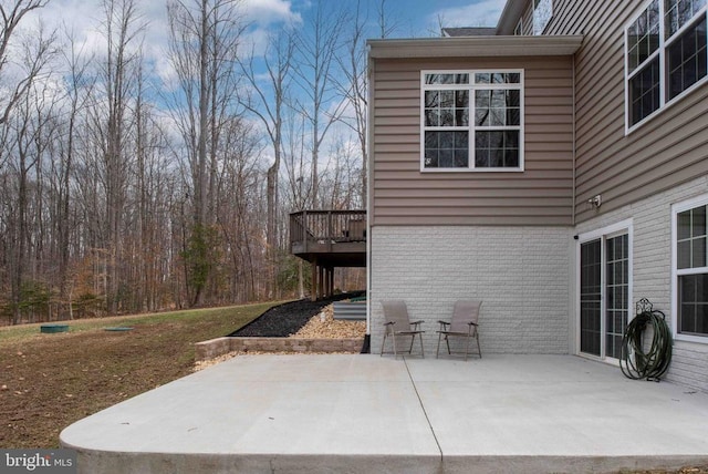 exterior space featuring brick siding, a wooden deck, and a patio