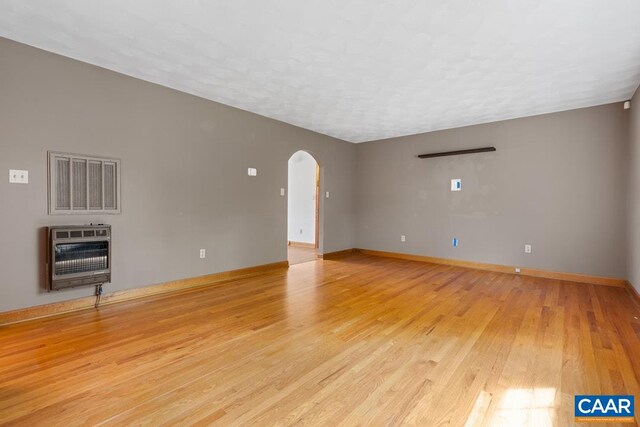 unfurnished living room with visible vents, heating unit, baseboards, arched walkways, and light wood-style flooring