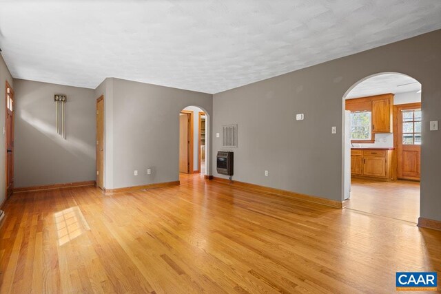 unfurnished living room with arched walkways, light wood-style flooring, baseboards, heating unit, and visible vents