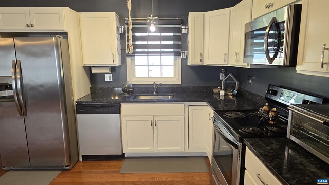 kitchen with sink, white cabinetry, appliances with stainless steel finishes, dark hardwood / wood-style flooring, and dark stone counters