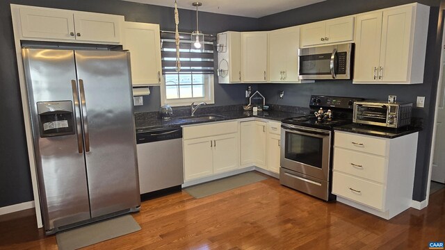 kitchen with appliances with stainless steel finishes, dark hardwood / wood-style floors, pendant lighting, sink, and white cabinets