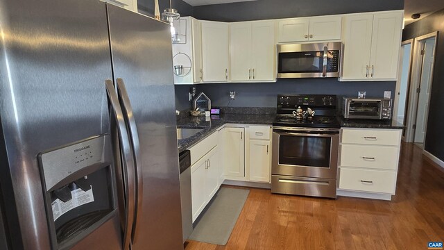 kitchen featuring dark stone countertops, hardwood / wood-style flooring, stainless steel appliances, and white cabinets